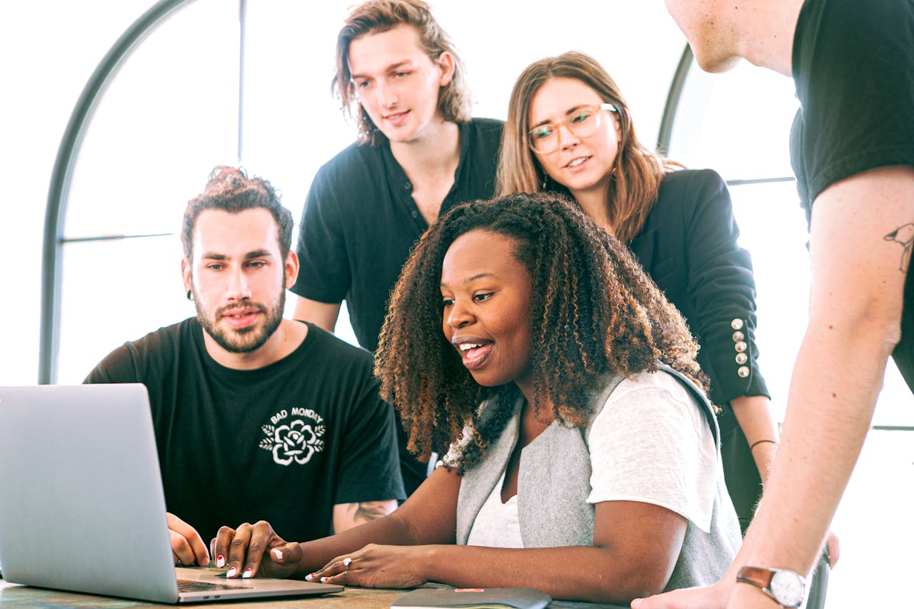 our-services-2 A diverse group of young professionals collaborating around a laptop in a modern office setting. Perfect for business or tech concepts.