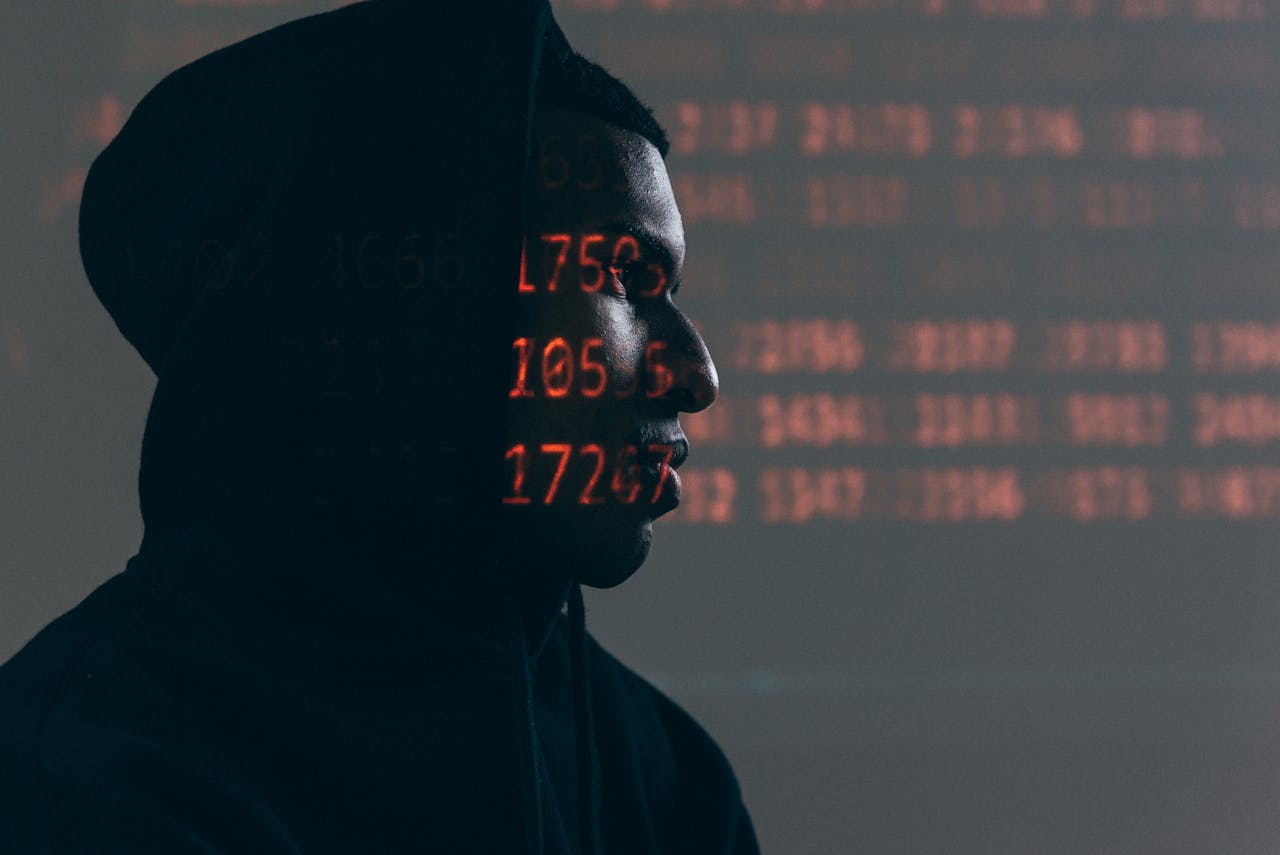 gallery-1 Side profile of a man in a hoodie, surrounded by red code, depicting cybersecurity theme.