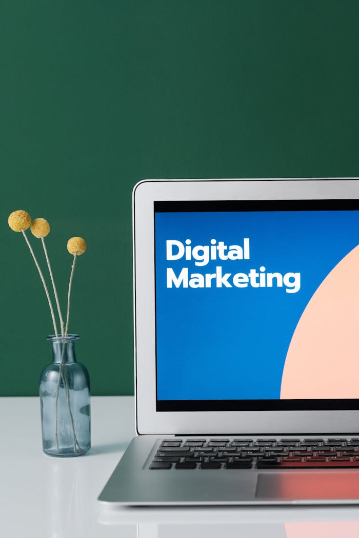 our-services-3 A laptop displaying 'Digital Marketing' with a minimalist floral decor in a glass vase.